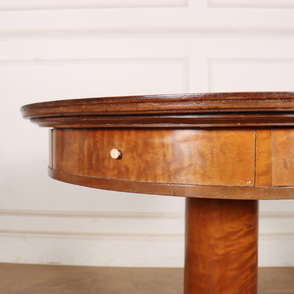 A 19th-century Swedish Biedermeier drum table in satin birch with a circular top, frieze drawers, central pedestal column, and four splayed legs. View V