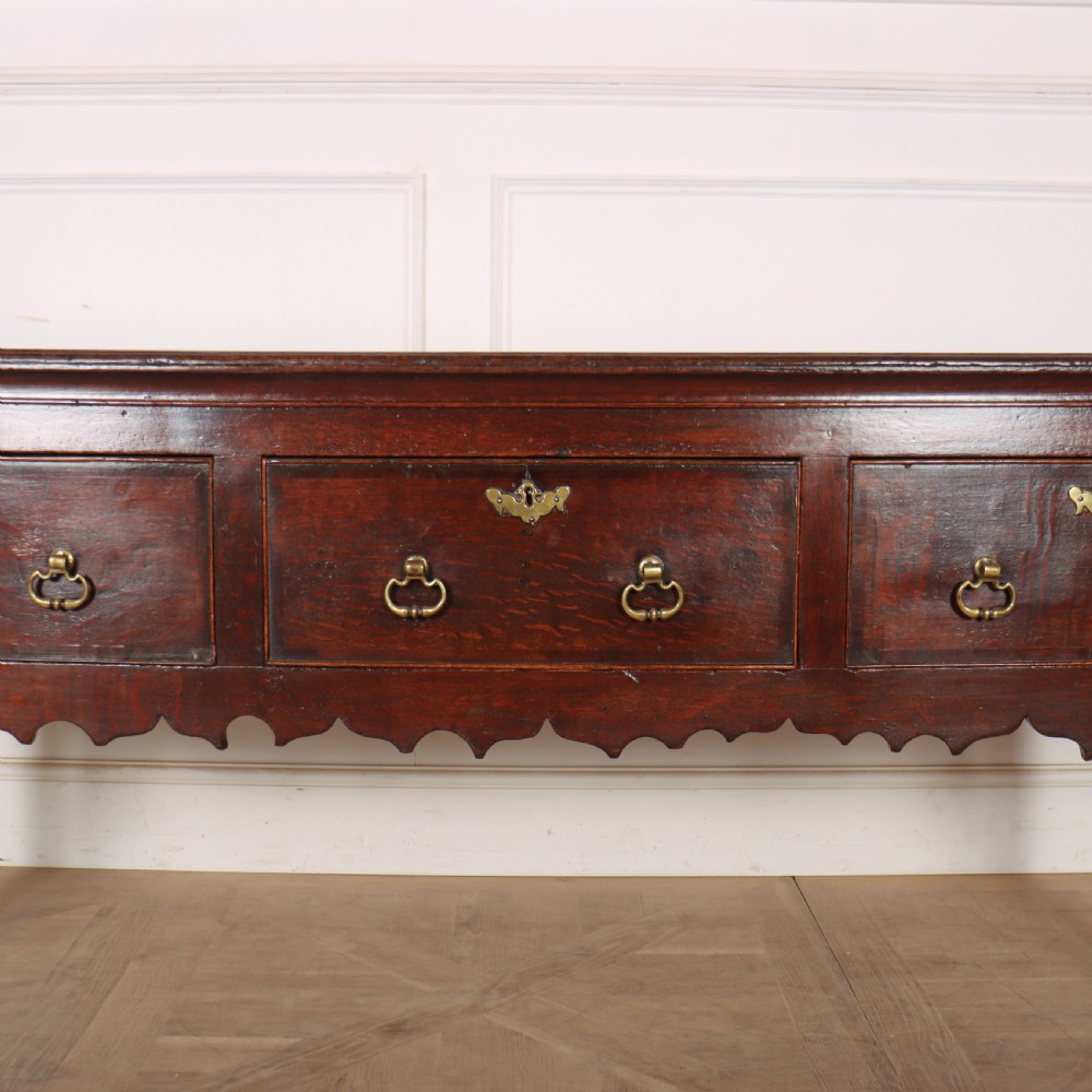 An 18th-century dark oak dresser base featuring three drawers, brass drop handles, keyhole escutcheons, a scalloped lower apron, and cabriole legs. View III