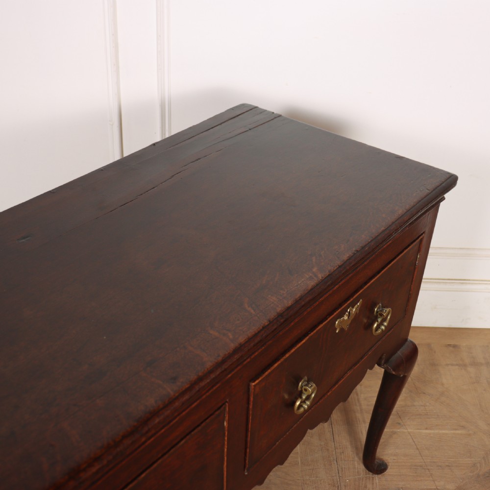 An 18th-century dark oak dresser base featuring three drawers, brass drop handles, keyhole escutcheons, a scalloped lower apron, and cabriole legs. View VII