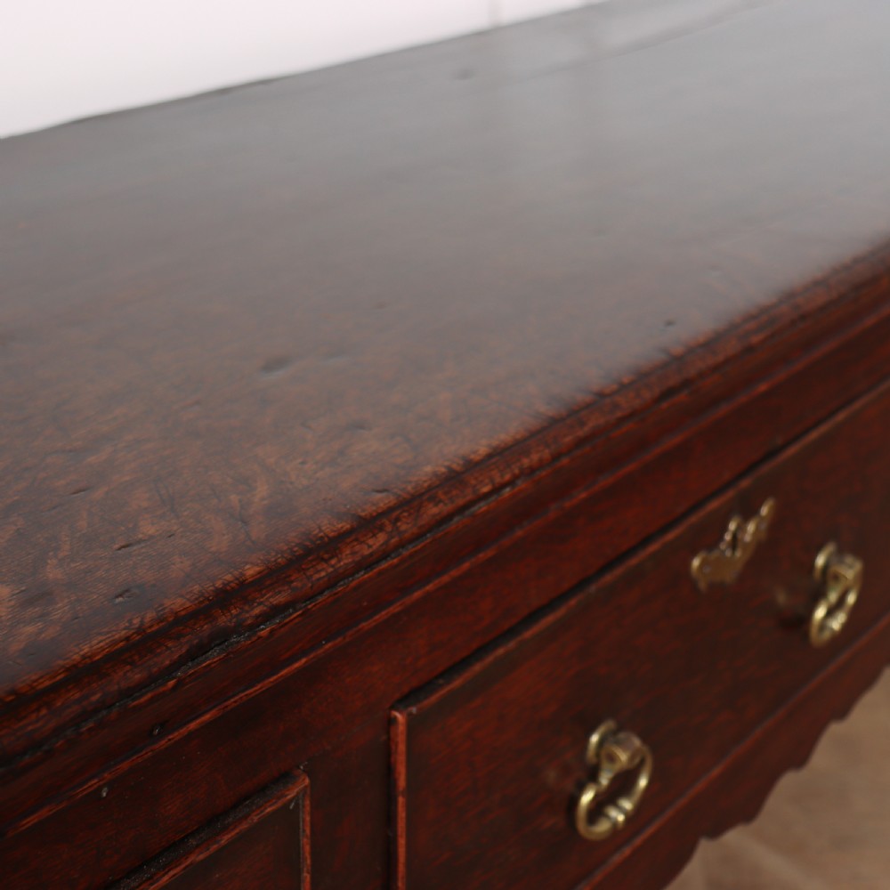 An 18th-century dark oak dresser base featuring three drawers, brass drop handles, keyhole escutcheons, a scalloped lower apron, and cabriole legs. View IX