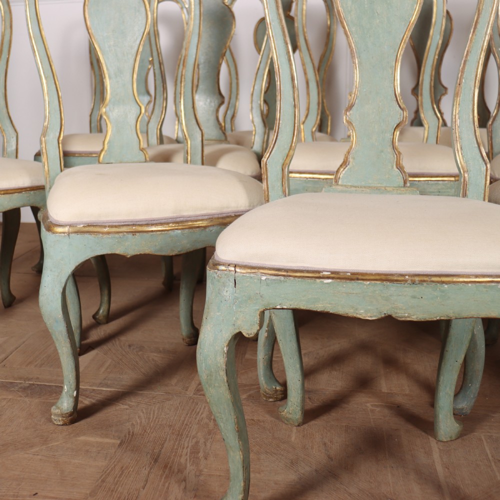 A set of twelve 18th-century Italian Rococo side chairs with pale green painted frames, parcel-gilt detailing, and cream upholstered seats. View V