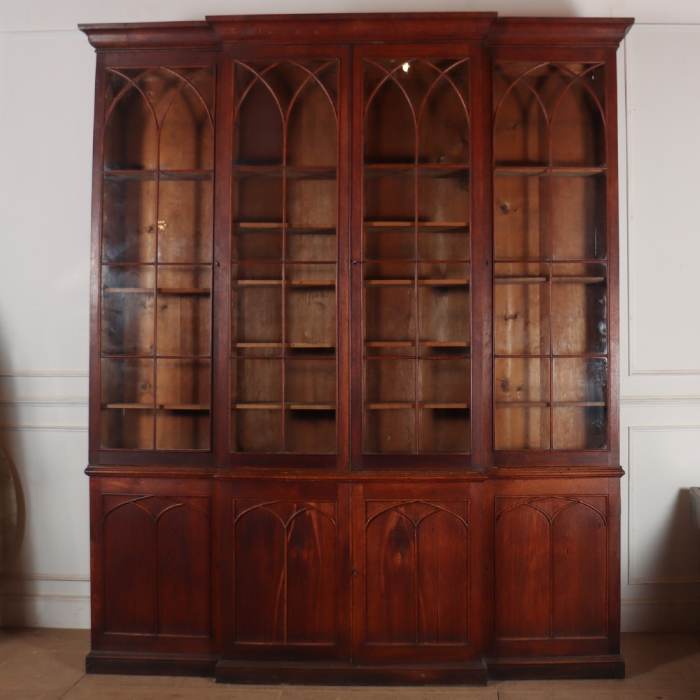 An early 19th-century mahogany breakfront bookcase featuring four glazed doors with Gothic pointed arch tracery over four matching panelled base doors.
