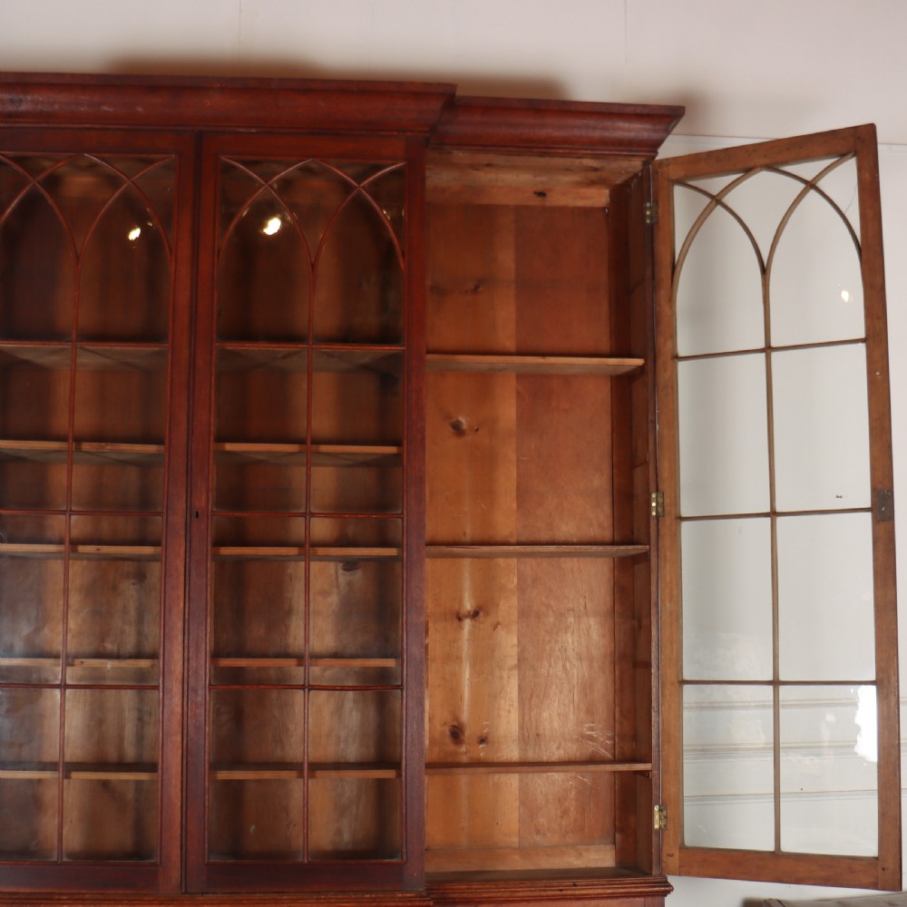An early 19th-century mahogany breakfront bookcase featuring four glazed doors with Gothic pointed arch tracery over four matching panelled base doors. View XV