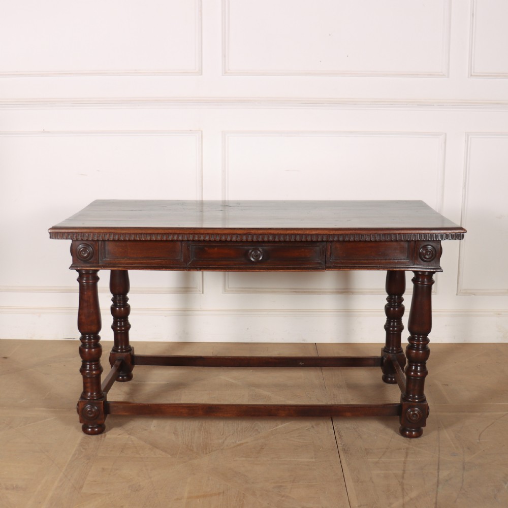 A 19th-century Italian dark walnut writing desk featuring turned legs, a carved frieze, a single central drawer, and a rectangular stretcher base.