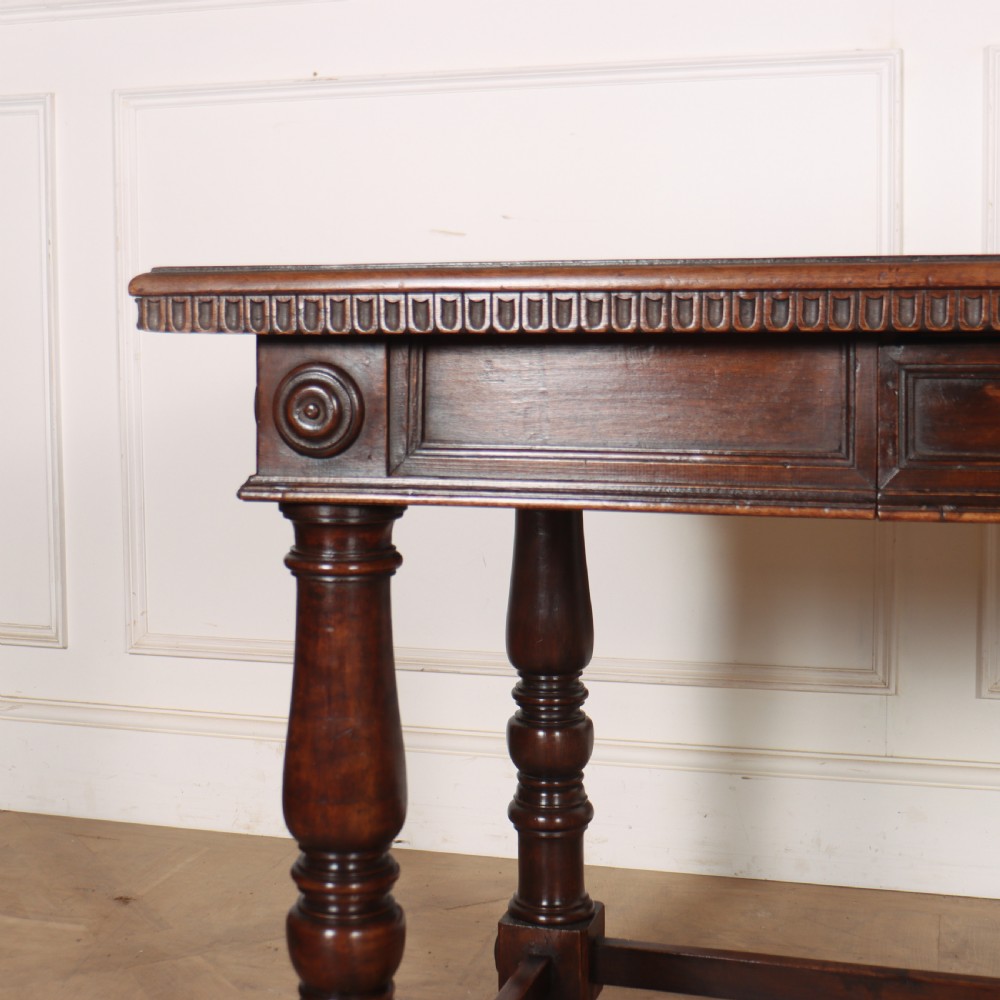 A 19th-century Italian dark walnut writing desk featuring turned legs, a carved frieze, a single central drawer, and a rectangular stretcher base. View II