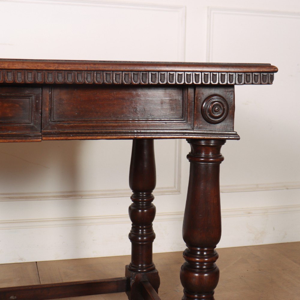 A 19th-century Italian dark walnut writing desk featuring turned legs, a carved frieze, a single central drawer, and a rectangular stretcher base. View IV