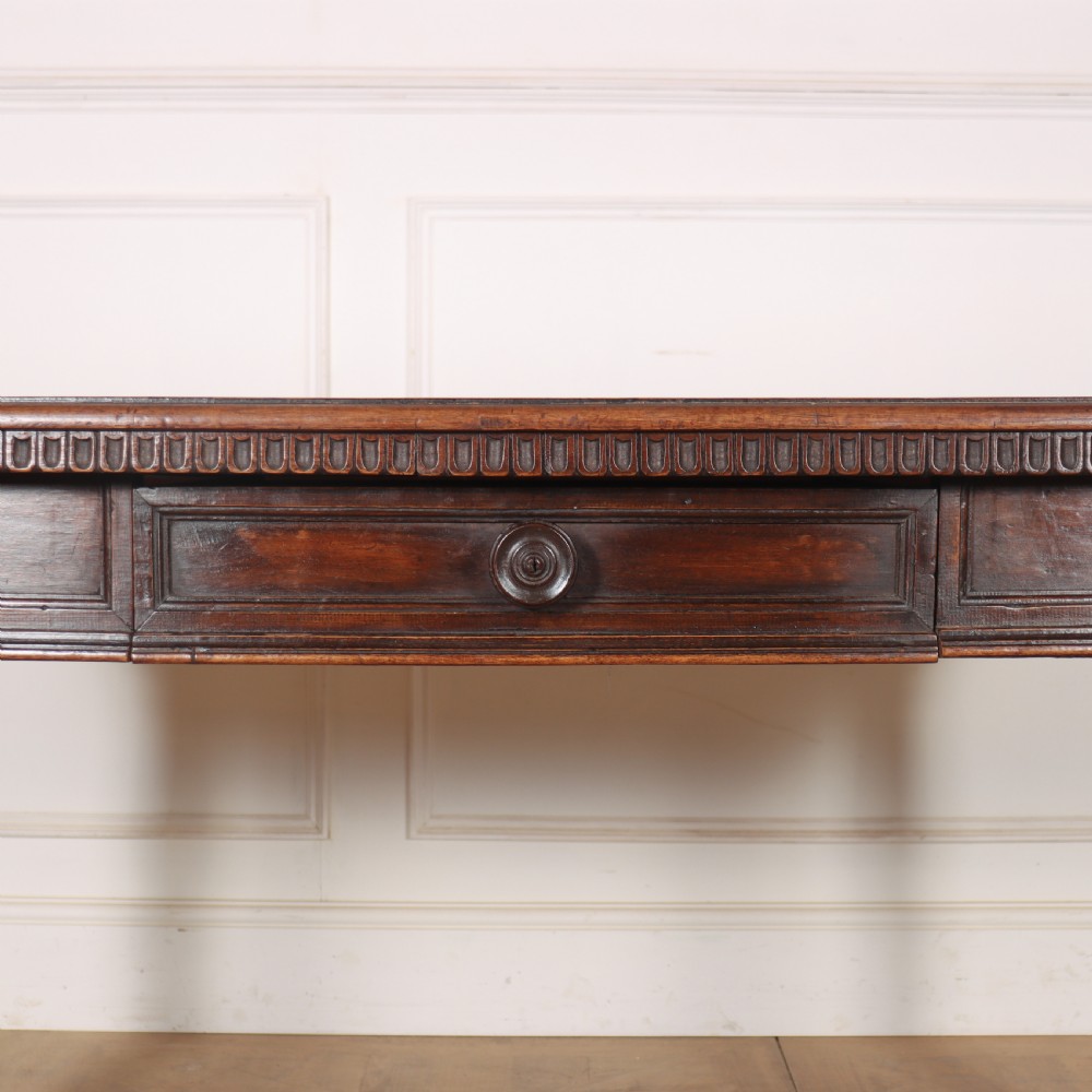 A 19th-century Italian dark walnut writing desk featuring turned legs, a carved frieze, a single central drawer, and a rectangular stretcher base. View V