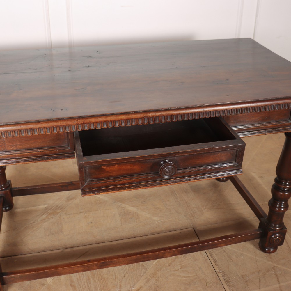 A 19th-century Italian dark walnut writing desk featuring turned legs, a carved frieze, a single central drawer, and a rectangular stretcher base. View VII