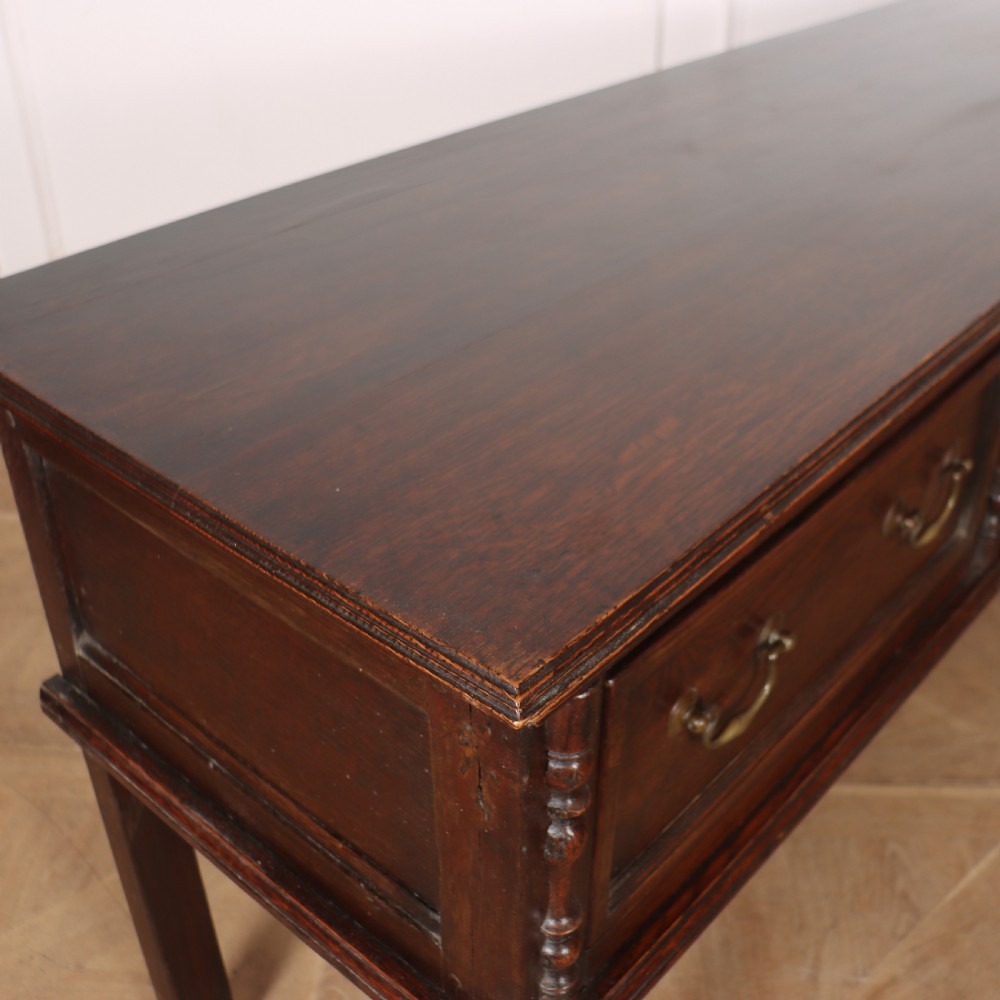 A dark oak dresser base featuring three panelled drawers with brass handles and turned front legs. View VII