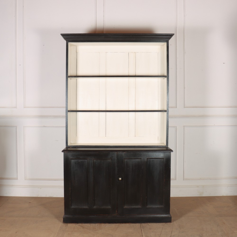 A 19th-century English painted open bookcase featuring a dark exterior, contrasting off-white interior shelves, and a lower two-door cupboard.