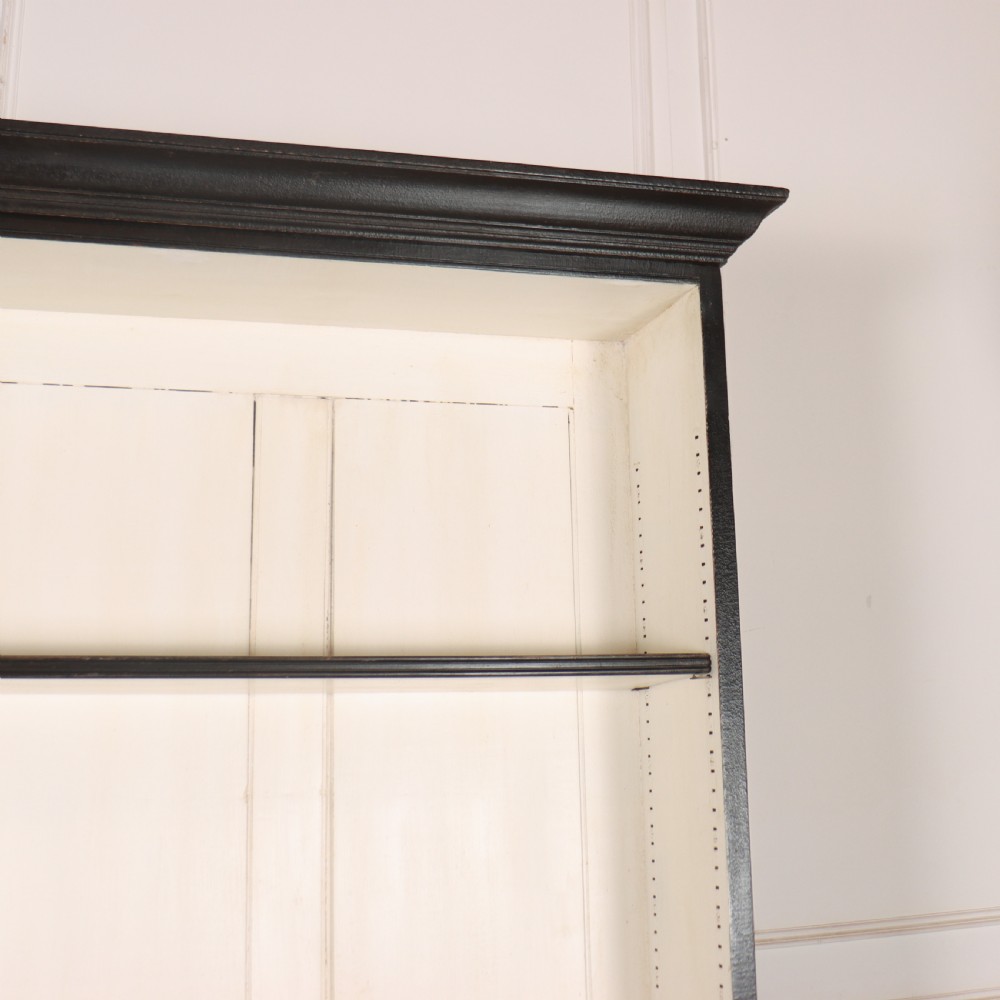 A 19th-century English painted open bookcase featuring a dark exterior, contrasting off-white interior shelves, and a lower two-door cupboard. View V