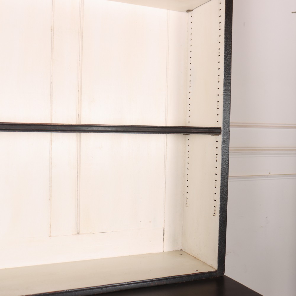 A 19th-century English painted open bookcase featuring a dark exterior, contrasting off-white interior shelves, and a lower two-door cupboard. View X