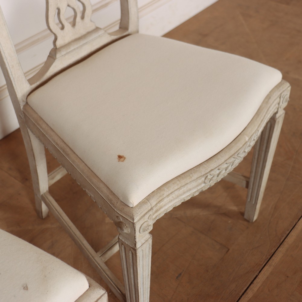 A set of six Gustavian style dining chairs painted in distressed off-white with carved splat backs and white upholstered seats. View VII