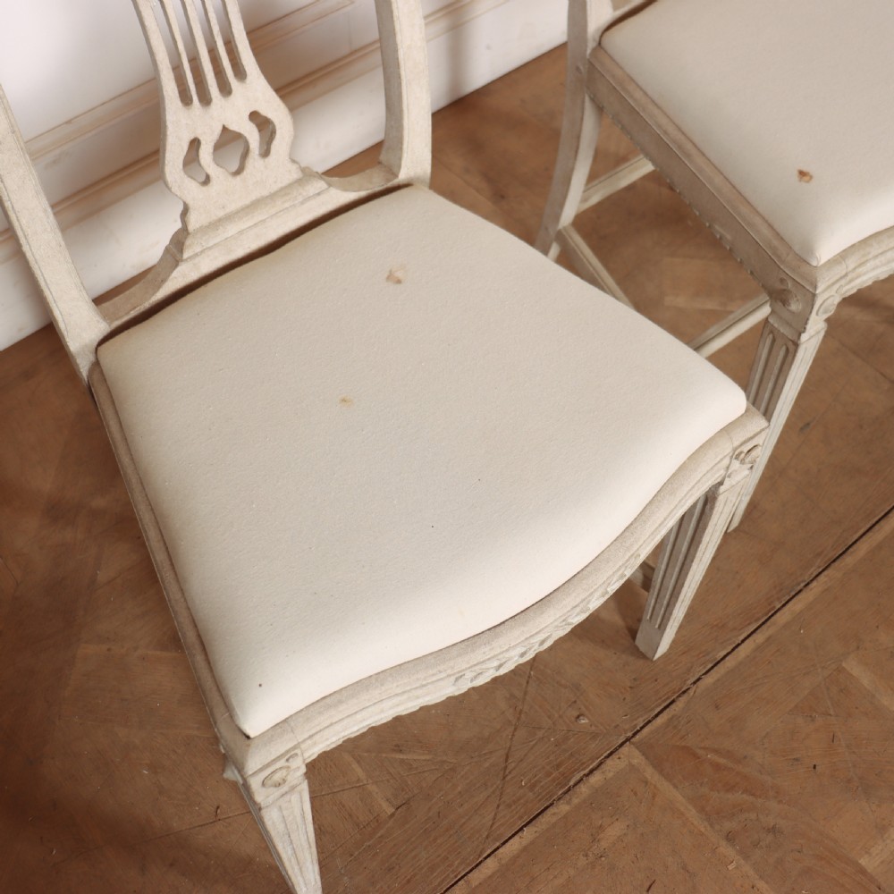 A set of six Gustavian style dining chairs painted in distressed off-white with carved splat backs and white upholstered seats. View VIII