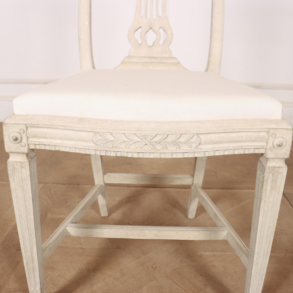 A set of six Gustavian style dining chairs painted in distressed off-white with carved splat backs and white upholstered seats. View X