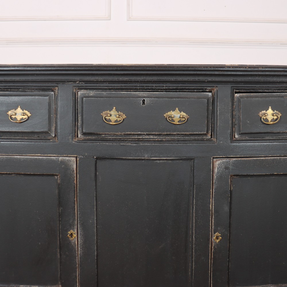 An 18th-century English country dresser base featuring a dark painted finish, three top drawers with brass handles, and three cupboard doors below. View II