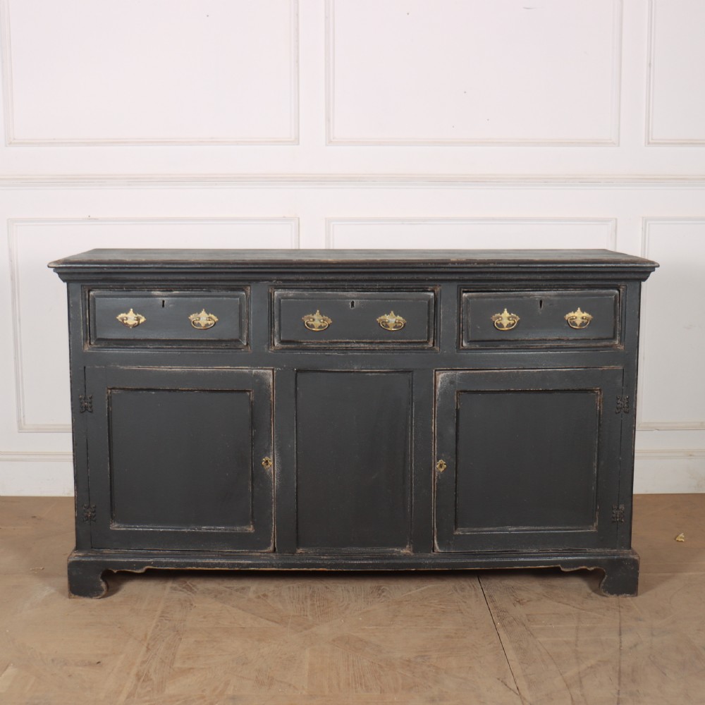 An 18th-century English country dresser base featuring a dark painted finish, three top drawers with brass handles, and three cupboard doors below.