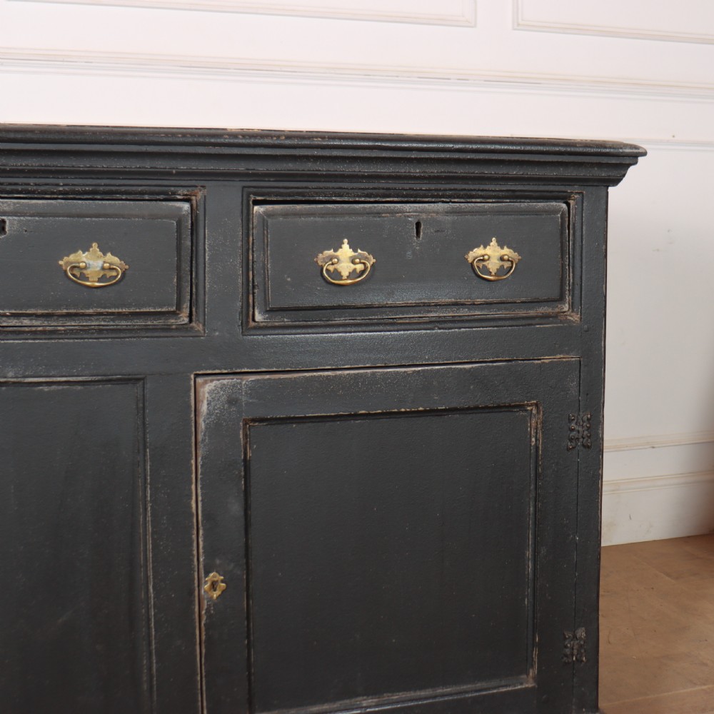 An 18th-century English country dresser base featuring a dark painted finish, three top drawers with brass handles, and three cupboard doors below. View IV