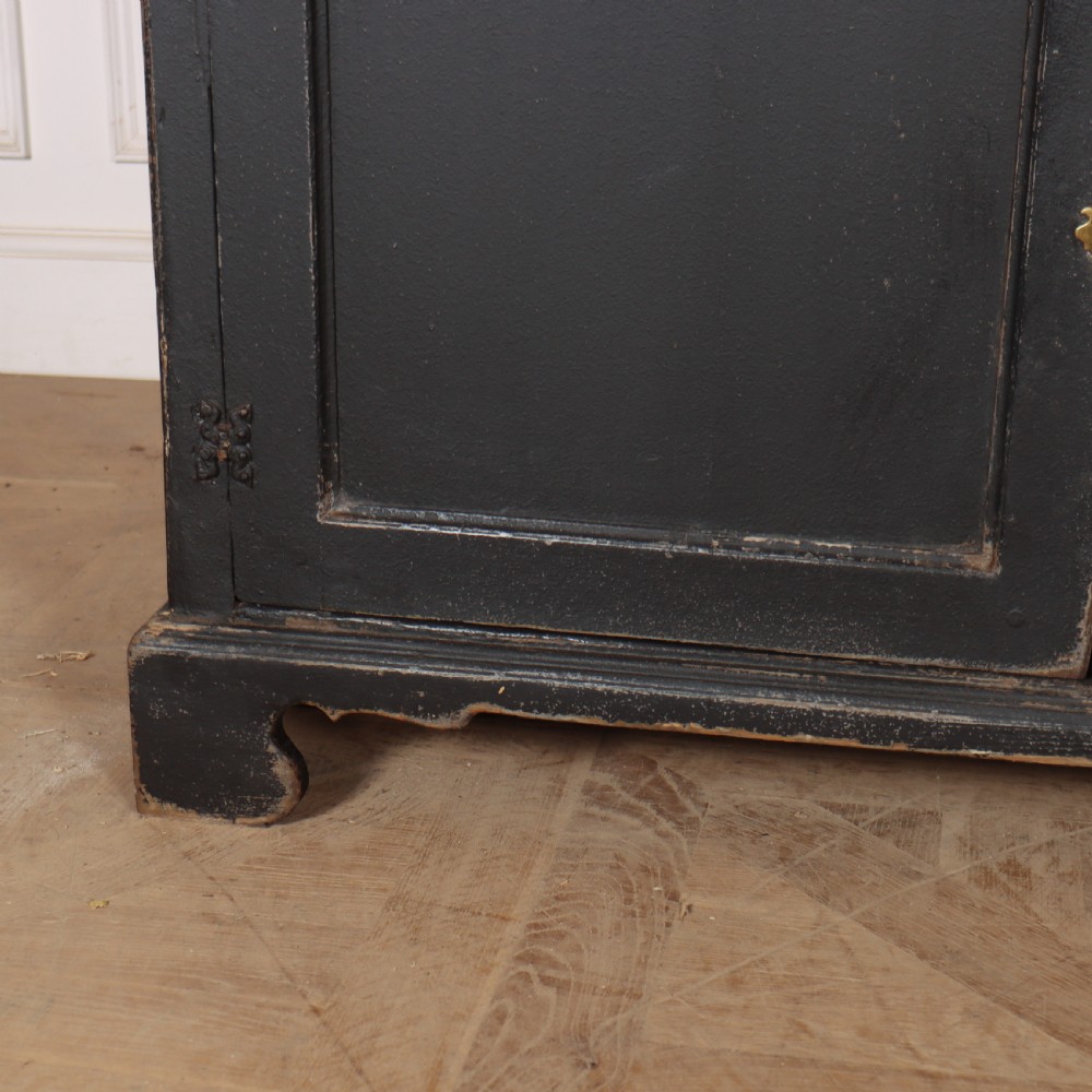 An 18th-century English country dresser base featuring a dark painted finish, three top drawers with brass handles, and three cupboard doors below. View V