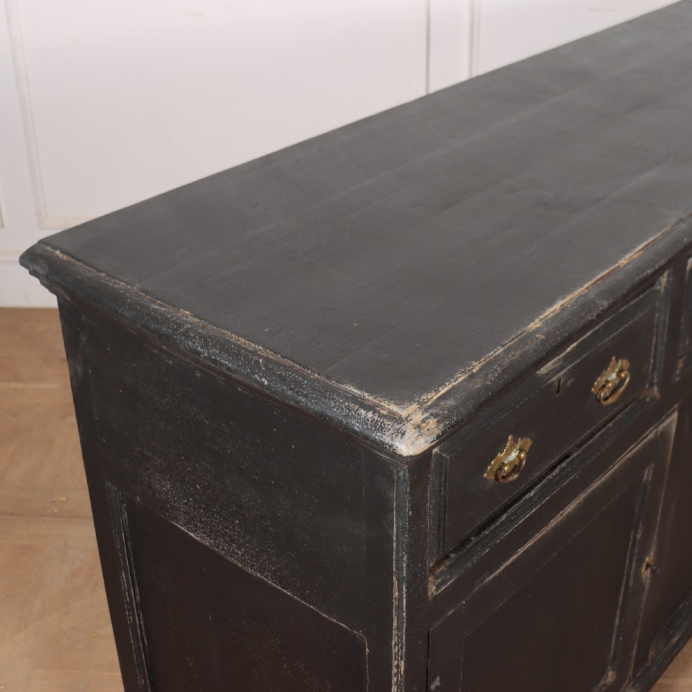 An 18th-century English country dresser base featuring a dark painted finish, three top drawers with brass handles, and three cupboard doors below. View X