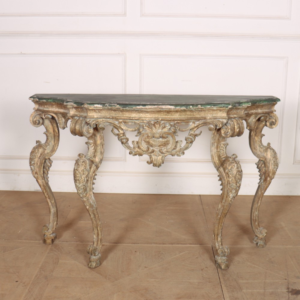 An 18th-century Italian carved giltwood console table featuring scrolled cabriole legs, a rocaille central apron, and a dark green marble top.