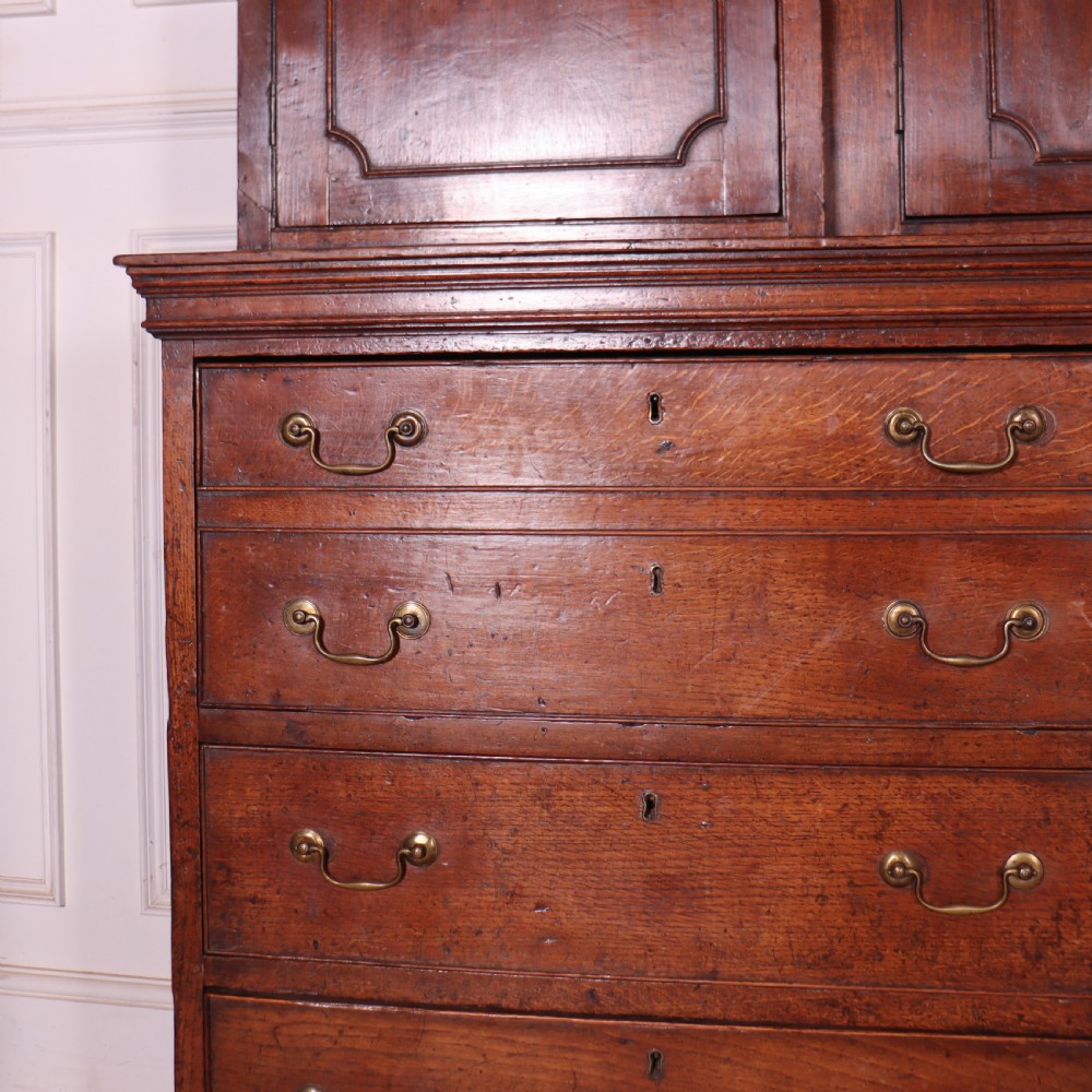 An antique English oak housekeepers cupboard featuring a breakfront upper section with fielded panel doors above a base with multiple drawers and brass hardware. View II