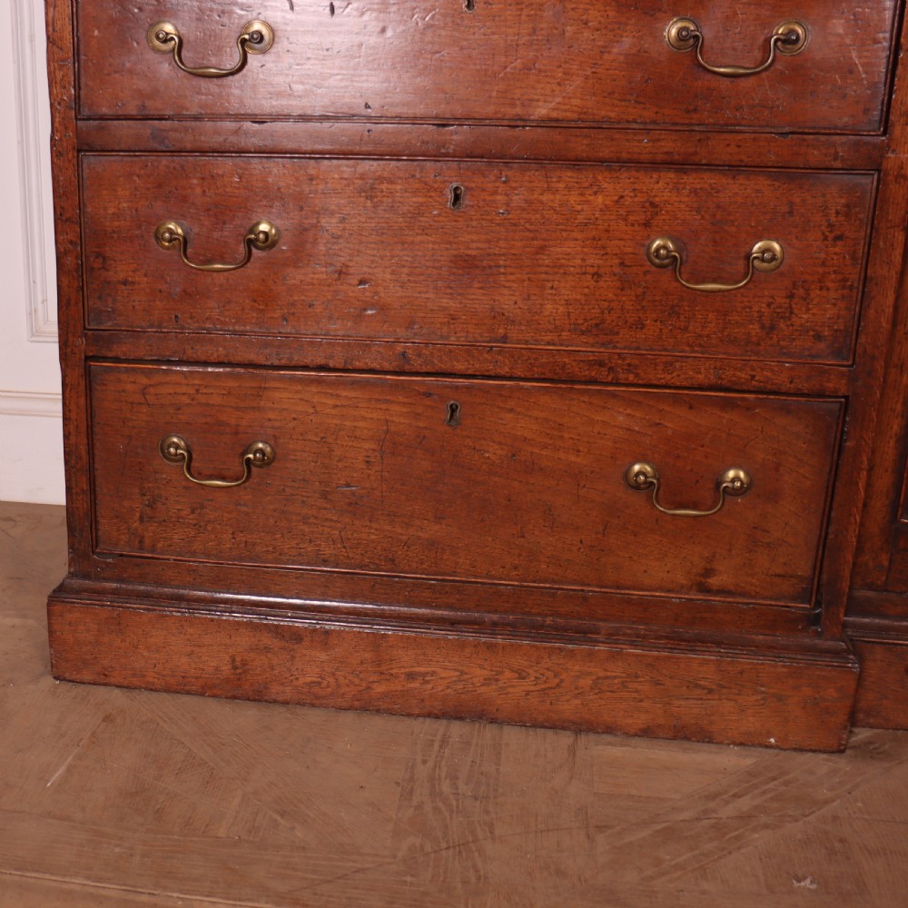 An antique English oak housekeepers cupboard featuring a breakfront upper section with fielded panel doors above a base with multiple drawers and brass hardware. View III