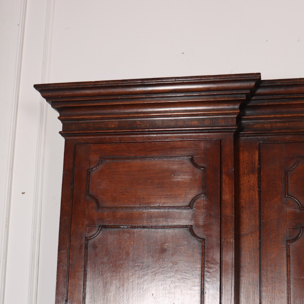 An antique English oak housekeepers cupboard featuring a breakfront upper section with fielded panel doors above a base with multiple drawers and brass hardware. View IV