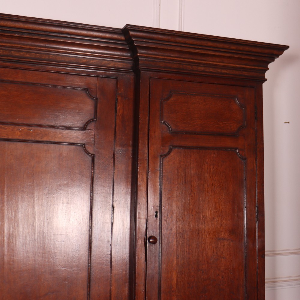 An antique English oak housekeepers cupboard featuring a breakfront upper section with fielded panel doors above a base with multiple drawers and brass hardware. View V