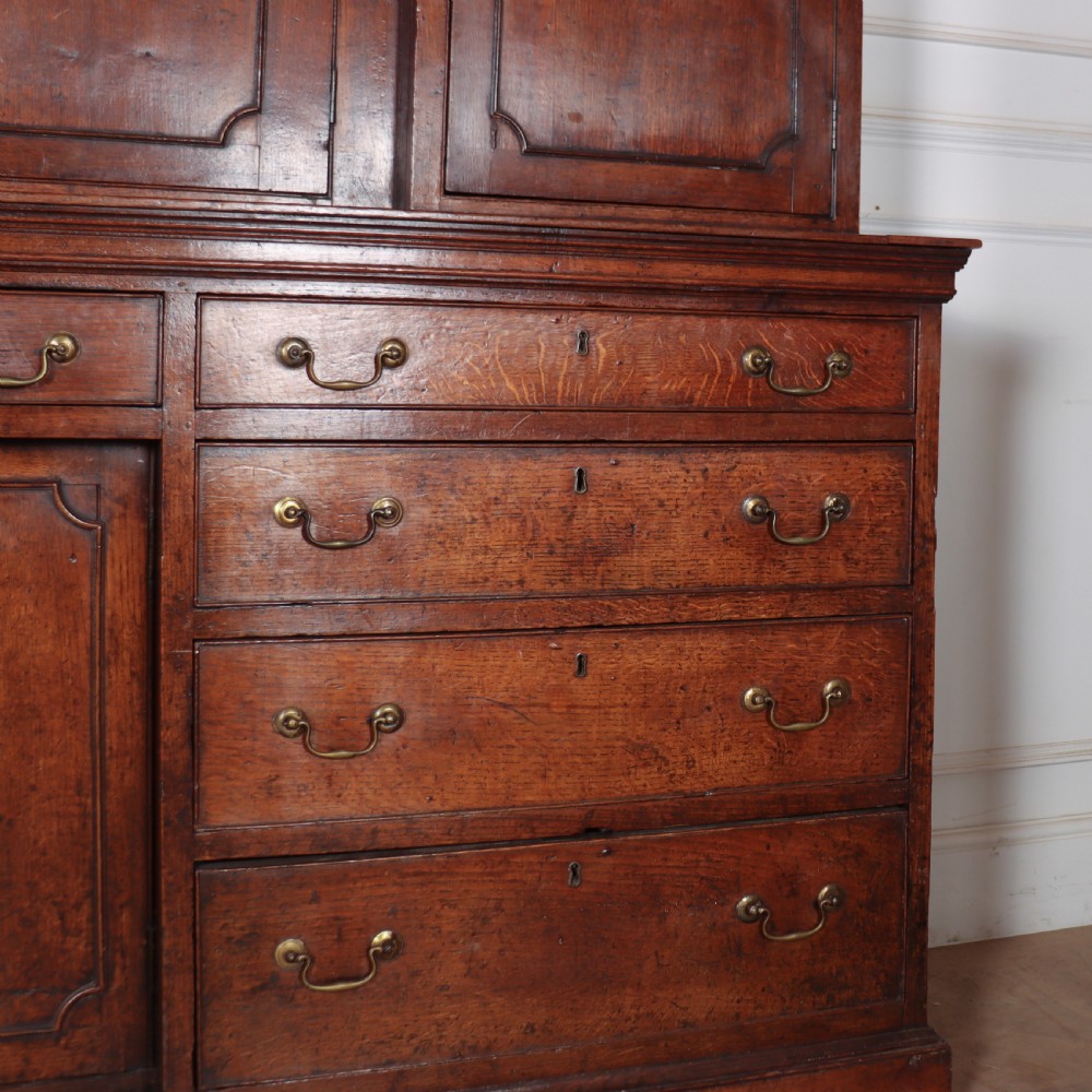An antique English oak housekeepers cupboard featuring a breakfront upper section with fielded panel doors above a base with multiple drawers and brass hardware. View VI