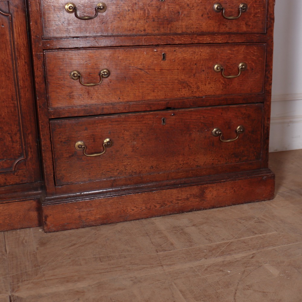 An antique English oak housekeepers cupboard featuring a breakfront upper section with fielded panel doors above a base with multiple drawers and brass hardware. View VII