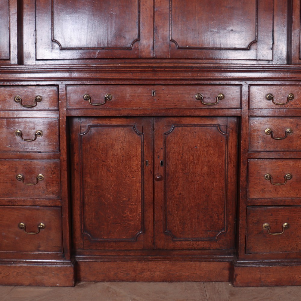 An antique English oak housekeepers cupboard featuring a breakfront upper section with fielded panel doors above a base with multiple drawers and brass hardware. View VIII