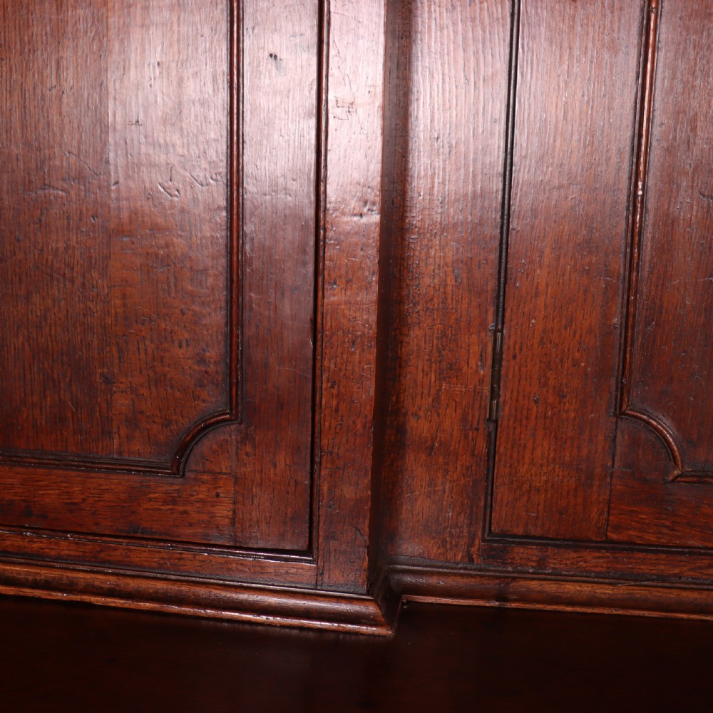An antique English oak housekeepers cupboard featuring a breakfront upper section with fielded panel doors above a base with multiple drawers and brass hardware. View IX