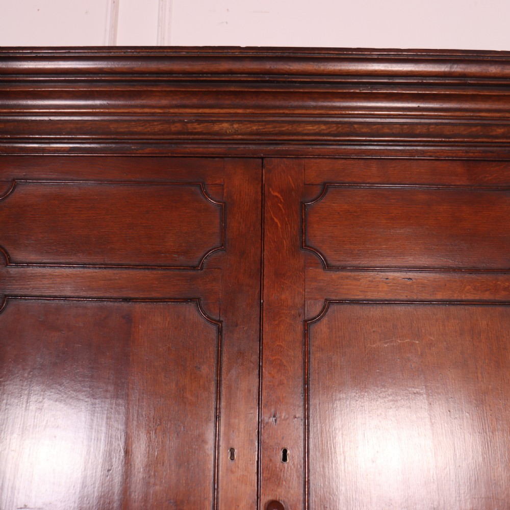 An antique English oak housekeepers cupboard featuring a breakfront upper section with fielded panel doors above a base with multiple drawers and brass hardware. View X