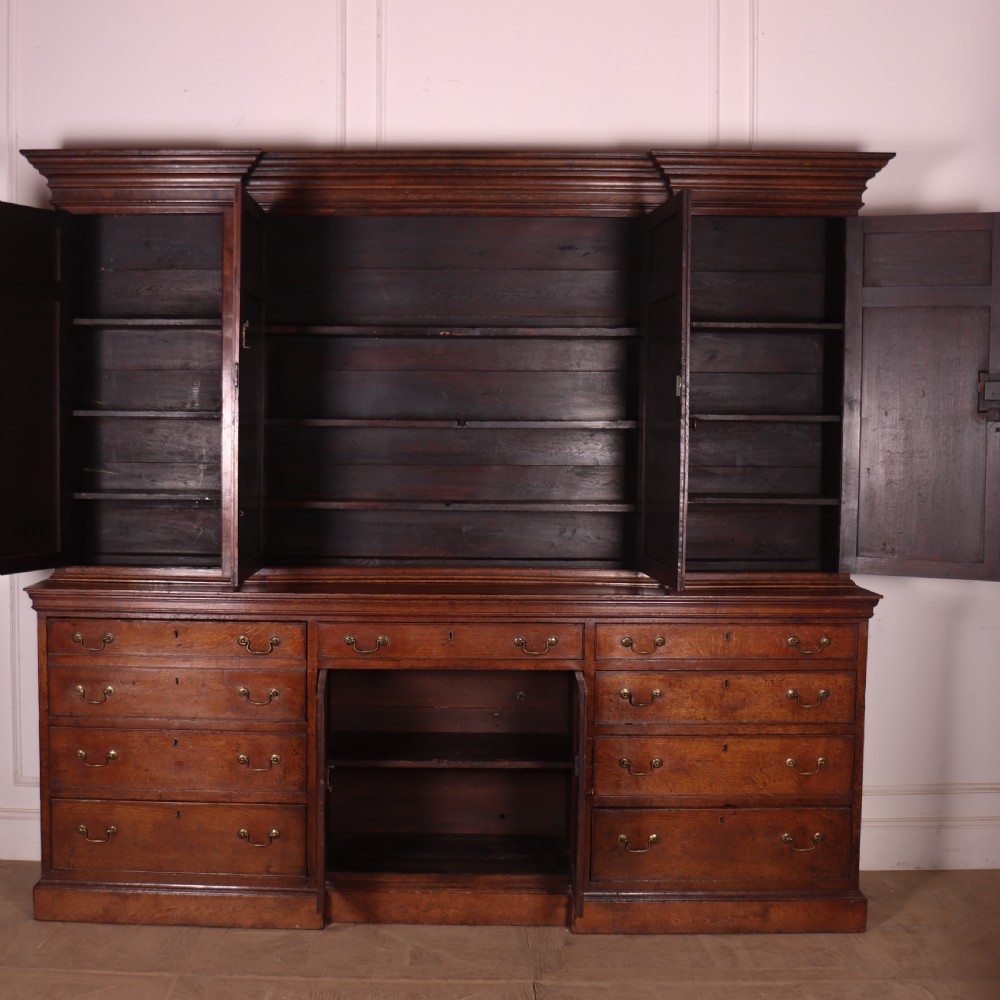 An antique English oak housekeepers cupboard featuring a breakfront upper section with fielded panel doors above a base with multiple drawers and brass hardware. View XI