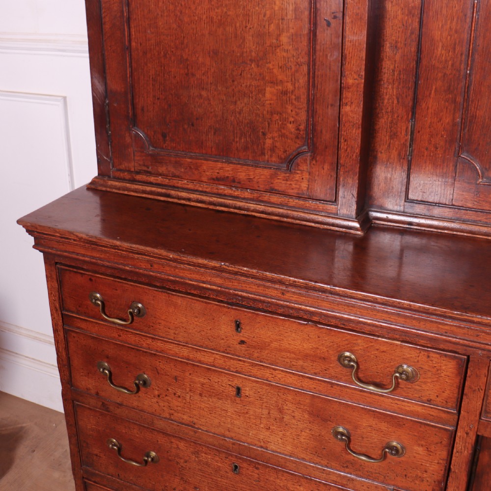 An antique English oak housekeepers cupboard featuring a breakfront upper section with fielded panel doors above a base with multiple drawers and brass hardware. View XII