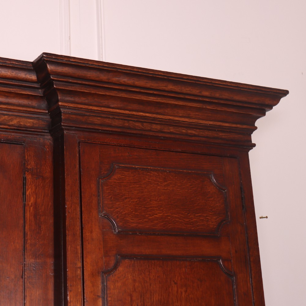 An antique English oak housekeepers cupboard featuring a breakfront upper section with fielded panel doors above a base with multiple drawers and brass hardware. View XIV