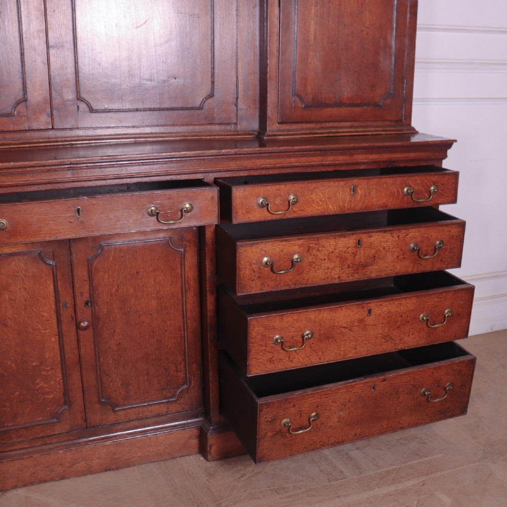 An antique English oak housekeepers cupboard featuring a breakfront upper section with fielded panel doors above a base with multiple drawers and brass hardware. View XVI