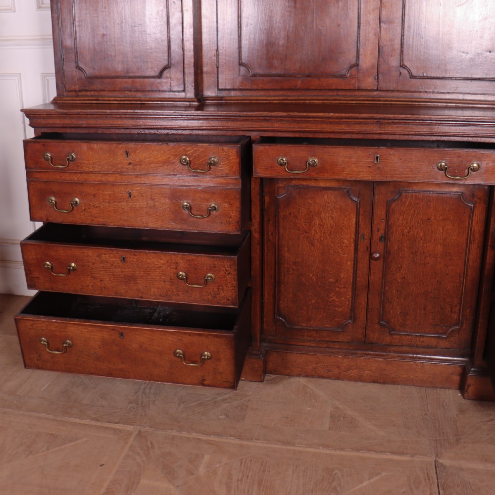 An antique English oak housekeepers cupboard featuring a breakfront upper section with fielded panel doors above a base with multiple drawers and brass hardware. View XVII