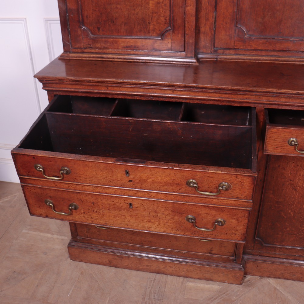 An antique English oak housekeepers cupboard featuring a breakfront upper section with fielded panel doors above a base with multiple drawers and brass hardware. View XVIII