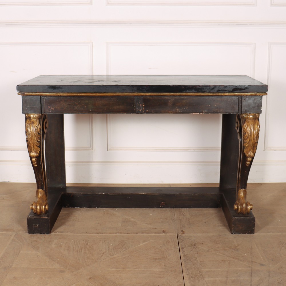 A dark painted and parcel-gilt console table featuring carved acanthus leaf scroll front supports and a flat plinth base.