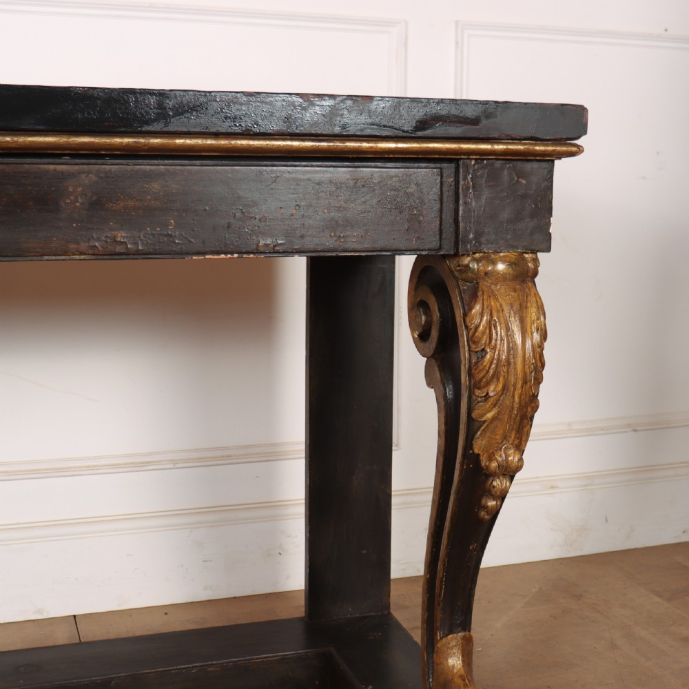 A dark painted and parcel-gilt console table featuring carved acanthus leaf scroll front supports and a flat plinth base. View V