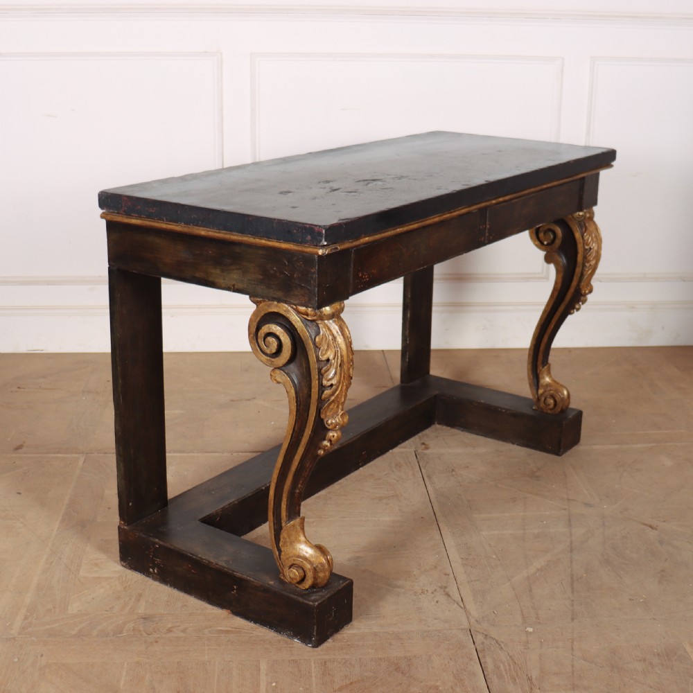 A dark painted and parcel-gilt console table featuring carved acanthus leaf scroll front supports and a flat plinth base. View VI