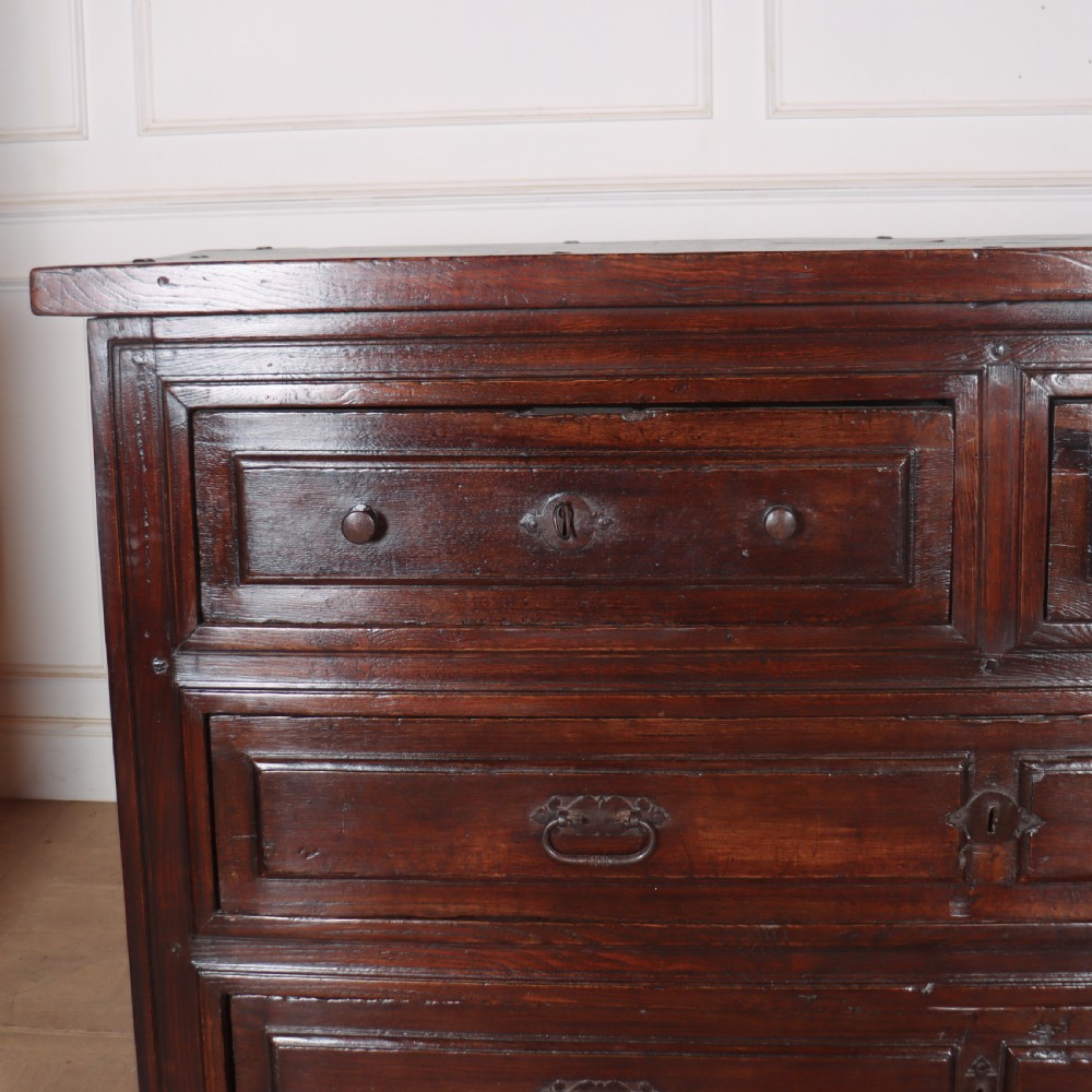 A large dark brown Spanish oak commode featuring deep geometric drawer mouldings, central lock escutcheons, and iron drop handles. View II
