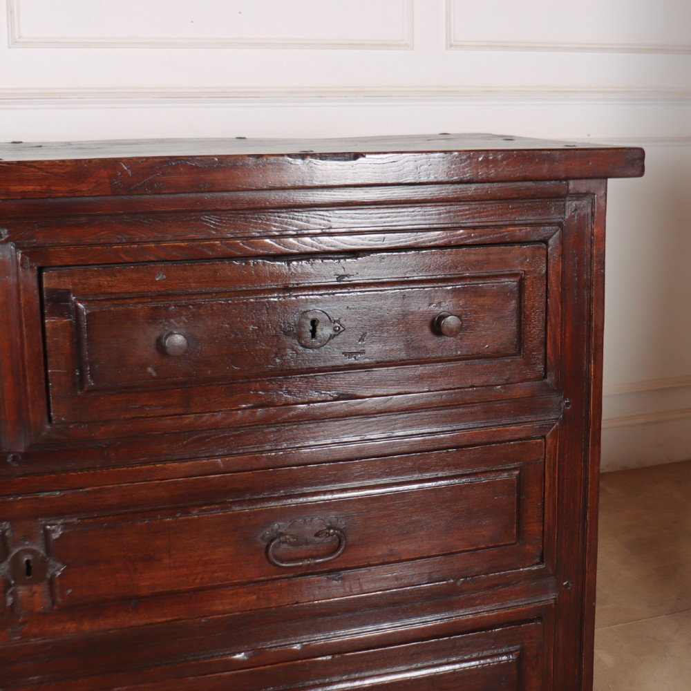 A large dark brown Spanish oak commode featuring deep geometric drawer mouldings, central lock escutcheons, and iron drop handles. View III