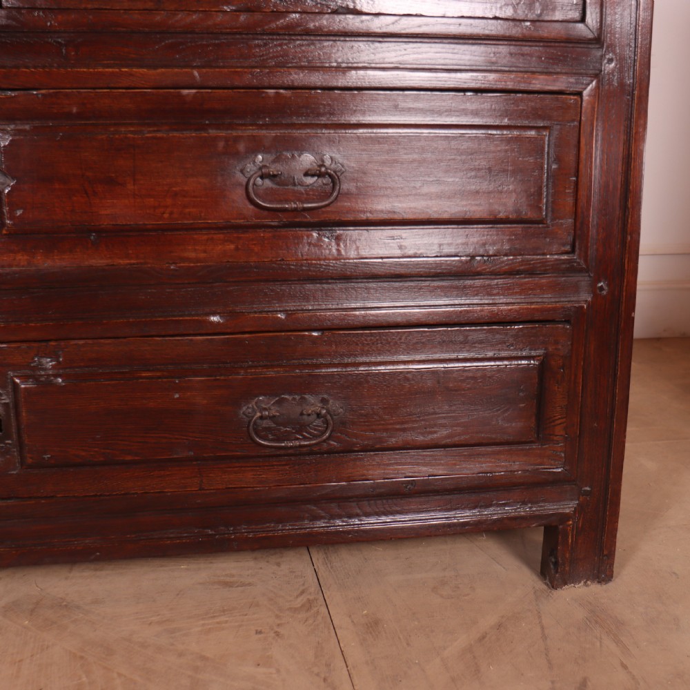 A large dark brown Spanish oak commode featuring deep geometric drawer mouldings, central lock escutcheons, and iron drop handles. View V