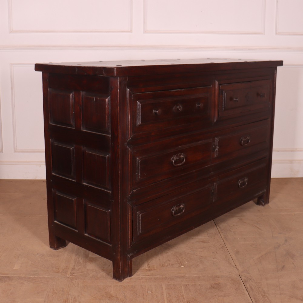 A large dark brown Spanish oak commode featuring deep geometric drawer mouldings, central lock escutcheons, and iron drop handles. View VI