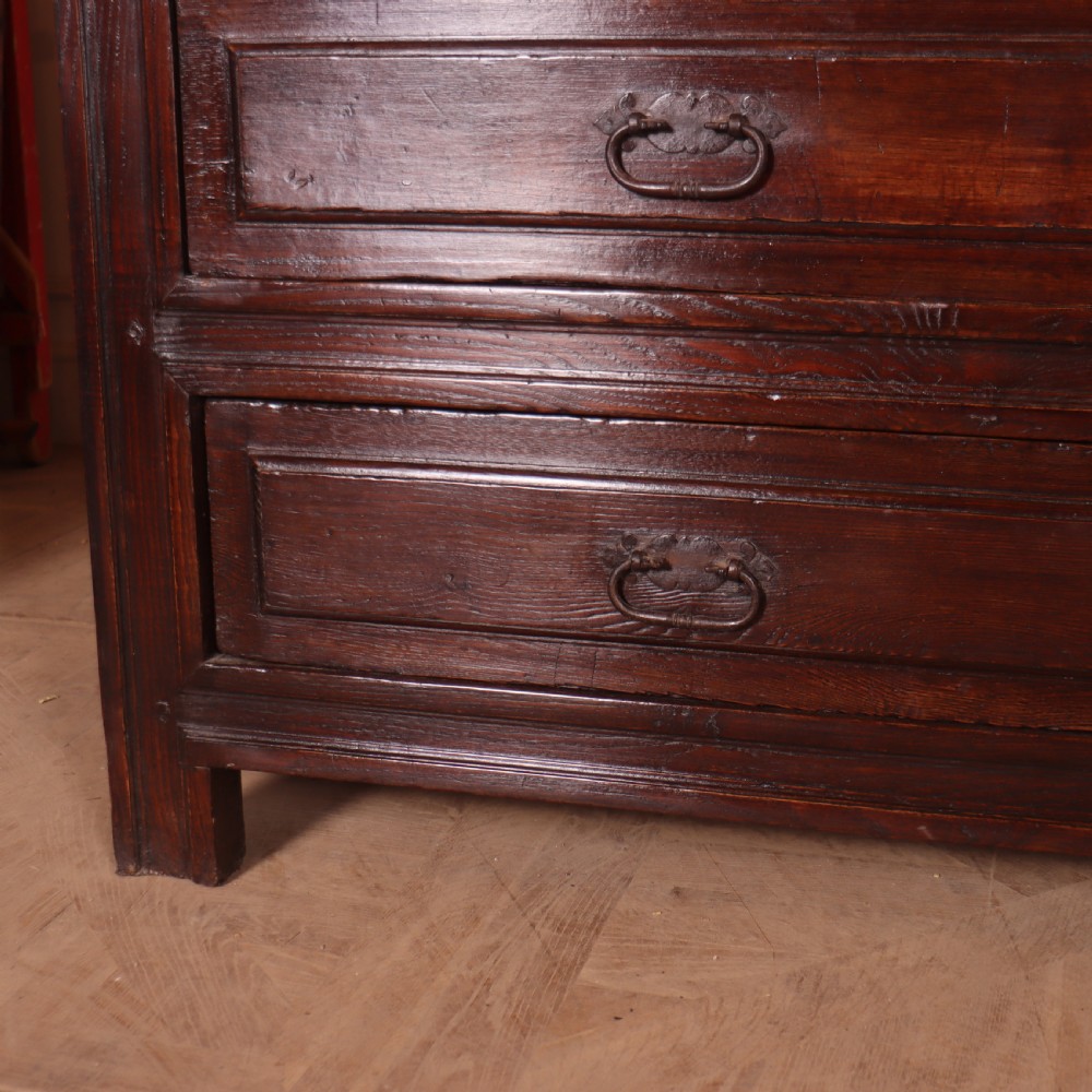 A large dark brown Spanish oak commode featuring deep geometric drawer mouldings, central lock escutcheons, and iron drop handles. View VII