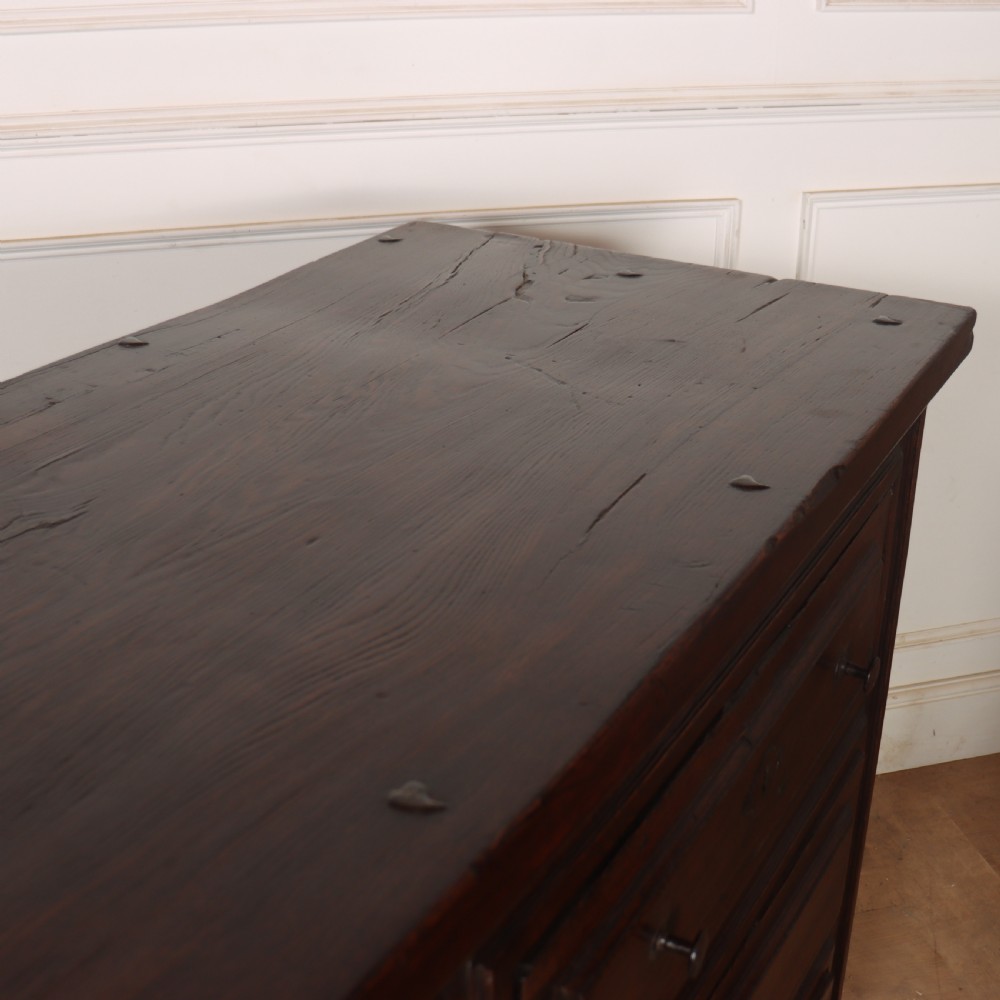 A large dark brown Spanish oak commode featuring deep geometric drawer mouldings, central lock escutcheons, and iron drop handles. View IX