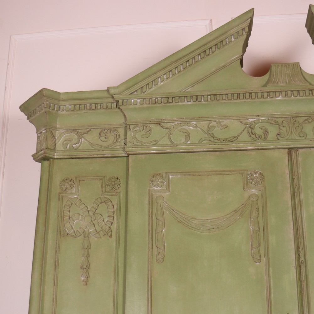 A large sage green painted Dutch linen cupboard featuring a broken pediment cornice, carved swag door panels, brass drop handles, and three lower drawers. View IV